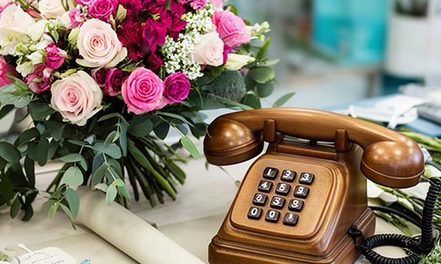 Teléfono antiguo junto a un ramo de flores frescas sobre una mesa de floristería en Manilva